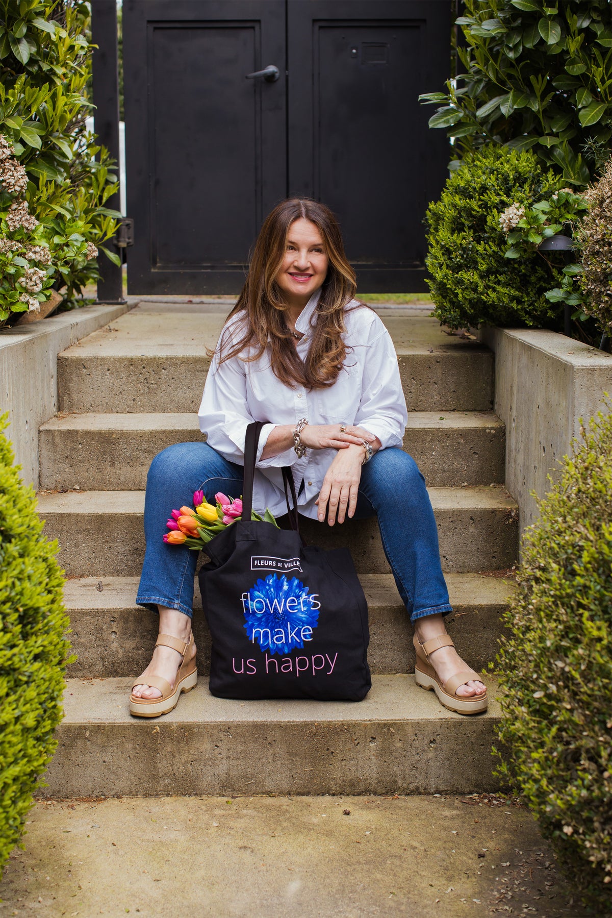 Karen Marshall sitting on steps with a tote bag featuring 'Flowers Make Us Happy' text.