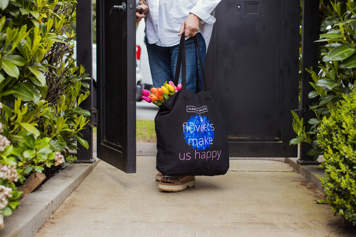 Person carrying a black tote bag with 'flowers make us happy' text, exiting a building.