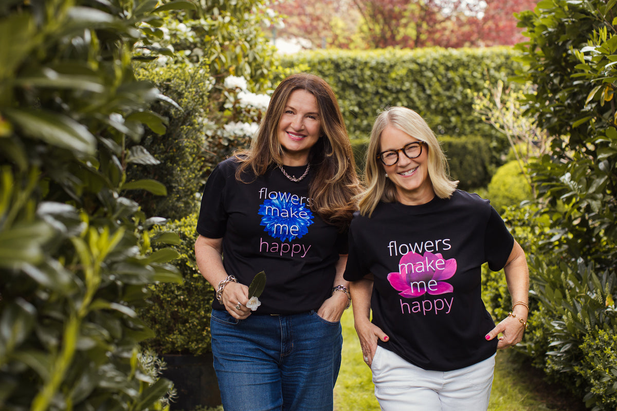 Karen & Tina wearing black "Flowers make me happy" t-shirts, standing outdoors. 