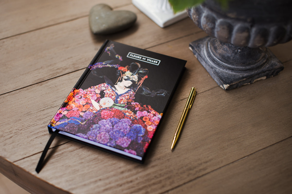 Notebook with floral mannequin on a wooden surface with a pen and decorative items.