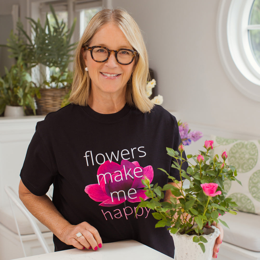 Tina Barkley wearing a black t-shirt with 'flowers make me happy' design, holding a potted plant.