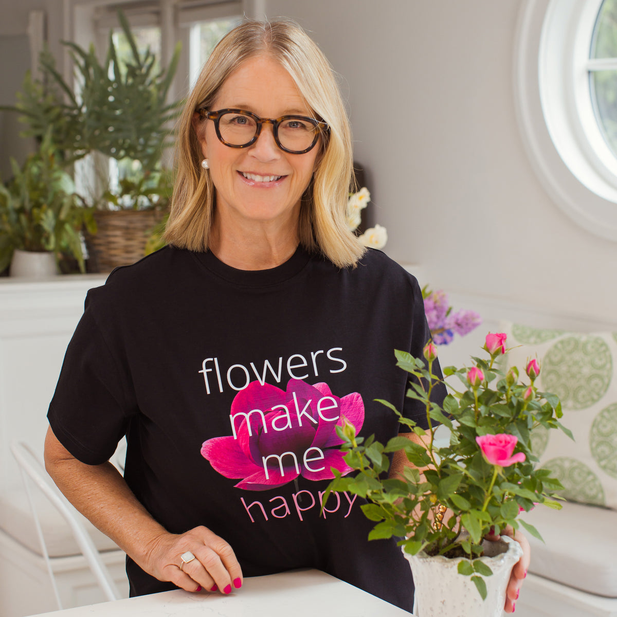 Tina Barkley wearing a black t-shirt with 'flowers make me happy' design, holding a potted plant.