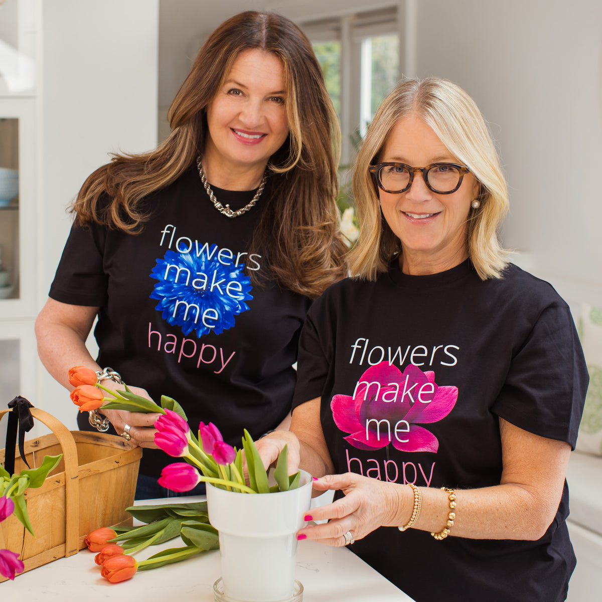 Two women wearing 'flowers make me happy' t-shirts, surrounded by flowers and a basket.