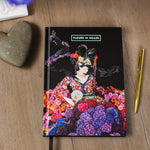 Notebook with colorful floral mannequin design on a wooden surface, featuring the brand 'Fleurs de Villes'.